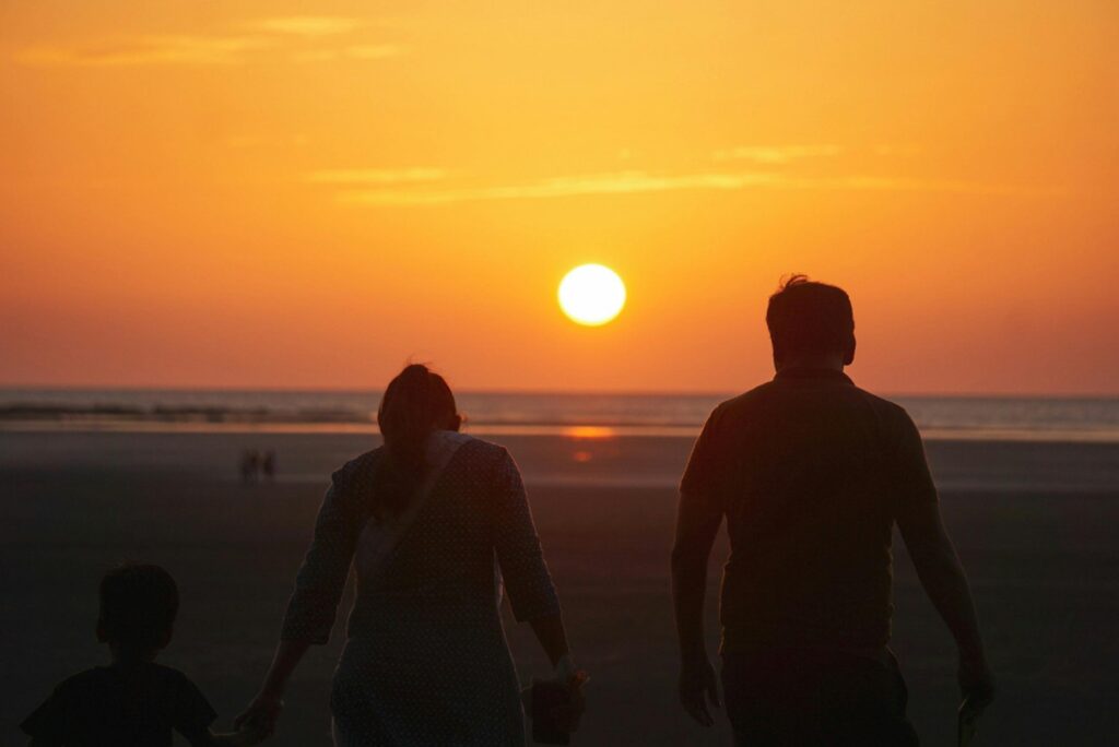 A family enjoys a serene sunset walk along the beach, captured in silhouette.