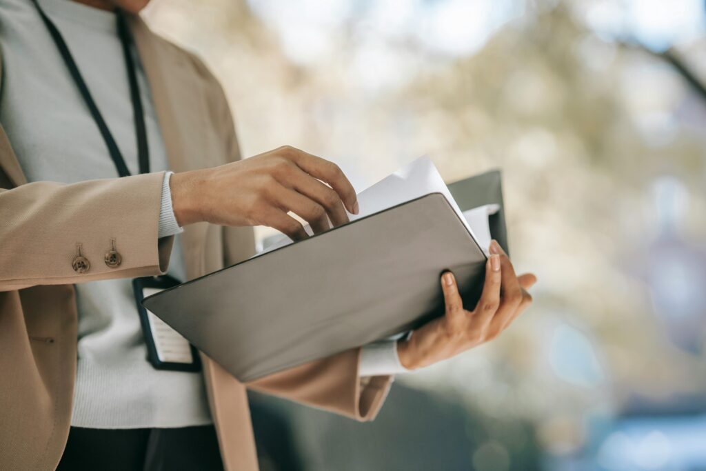 Crop anonymous female entrepreneur in elegant jacket with badge looking through papers in folder