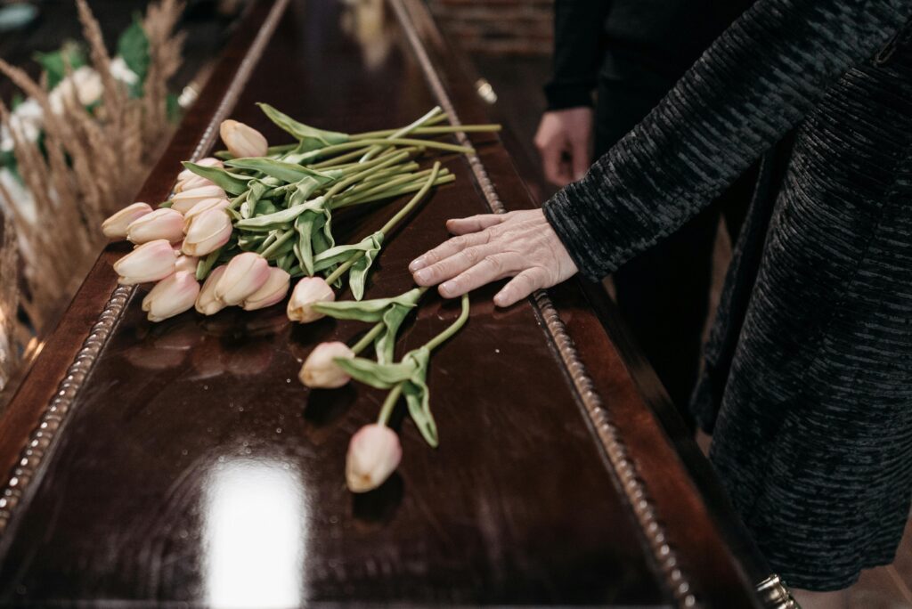 A somber funeral scene with tulips placed on a wooden coffin, symbolizing loss and remembrance.