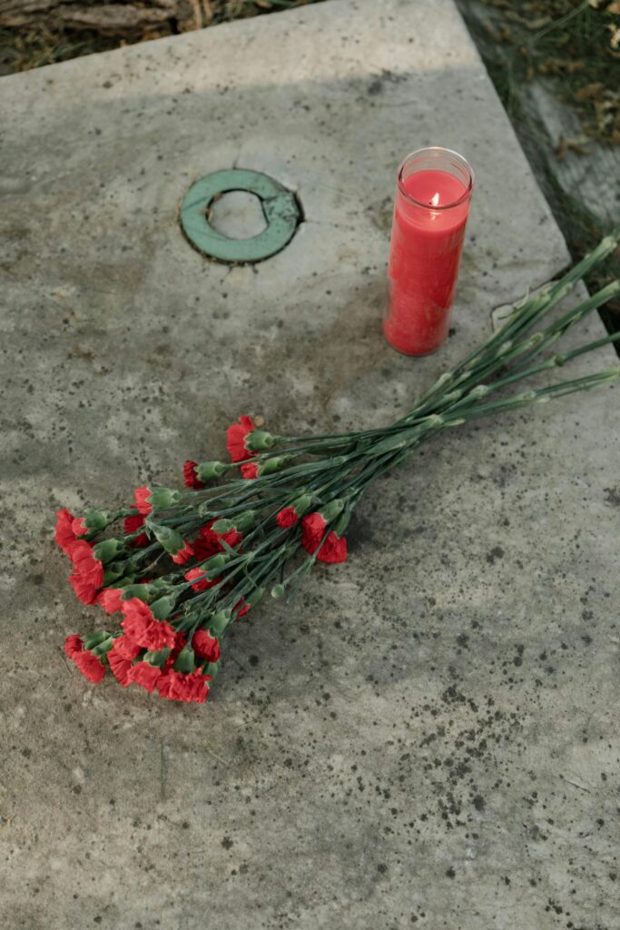 A serene vertical shot of red carnations and candle on a gravestone.
